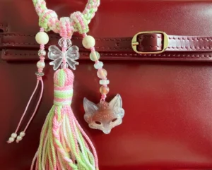 Agate fox spirit bag charm and Chinese keychain hanging from a burgundy leather handbag with butterfly bead braided pink green cord and tassel
