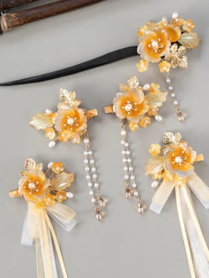 Overhead view of a vintage amber camellia Hanfu hair accessories set with gold-tone leaves, faux pearl centers, beaded tassels, and champagne sheer ribbon bows