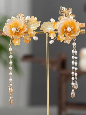 Pair of amber camellia Hanfu hair clips with gold-tone details, faux pearls, and long crystal-style tassels displayed on a stand