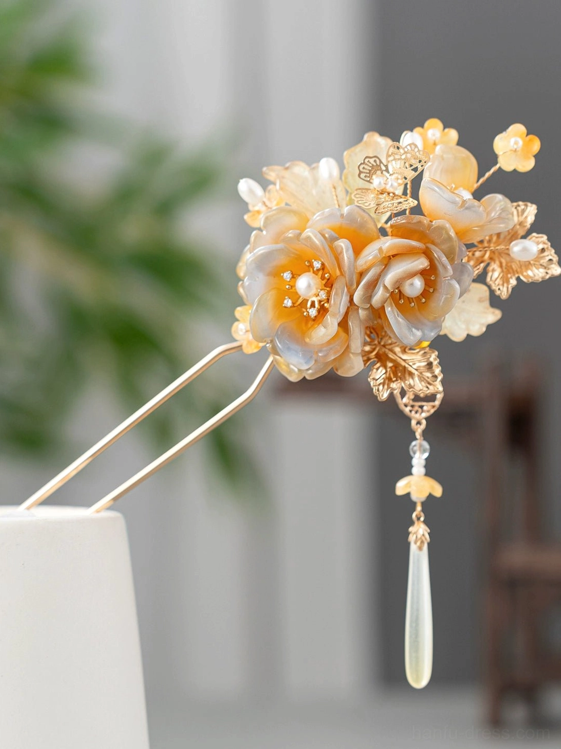 Close-up of an amber gradient Chinese hairpin with floral resin details, gold-tone embellishments, and a long jade-like water-drop pendant for Hanfu hairstyles