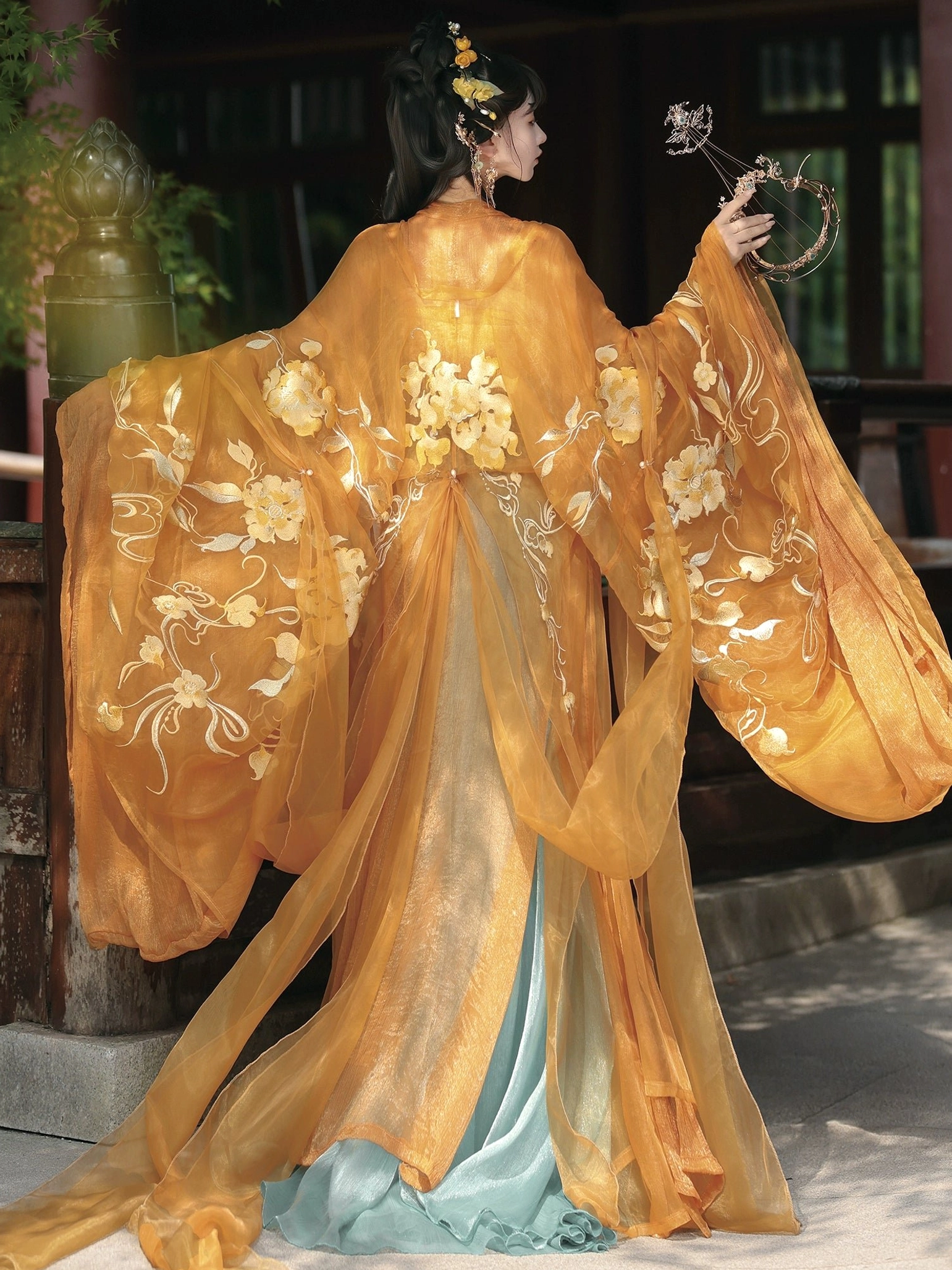 Back view of amber orange Tang Dynasty hanfu Qixiong Ruqun with golden floral embroidery, wide decorated sleeves, layered color block skirt, and traditional Chinese styling