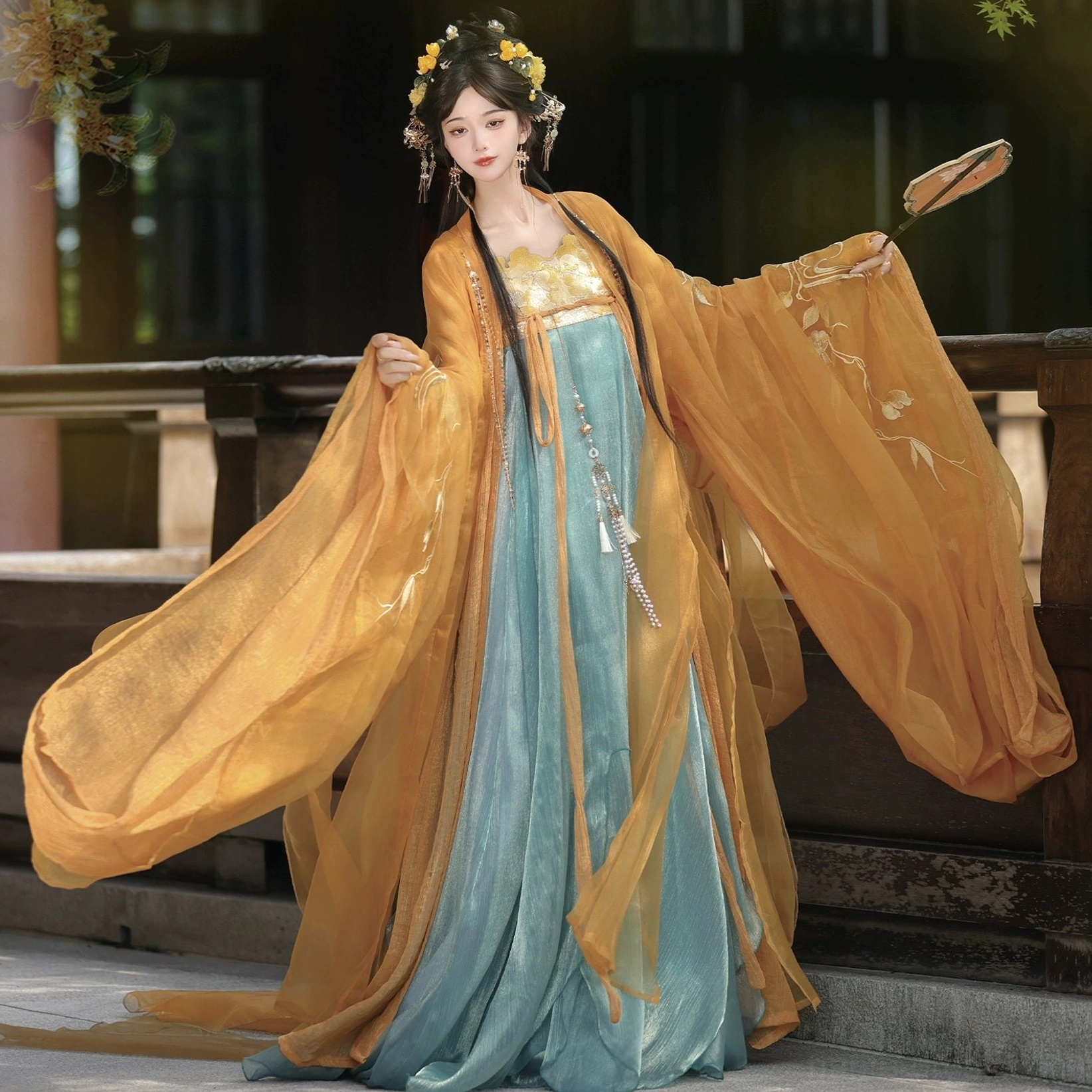 Amber orange Tang Dynasty Qixiong Ruqun complete hanfu set shown from the front with wide chiffon sleeves, golden bustier top, teal floor length skirt, sash, and tassel waist pendant