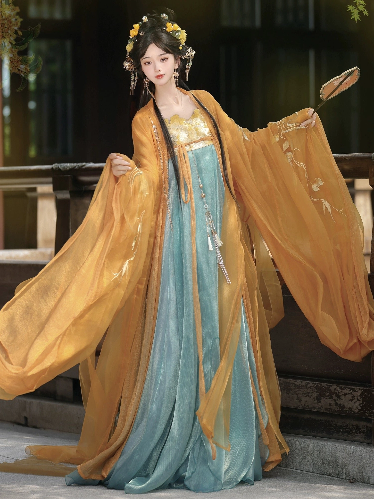 Amber orange Tang style Qixiong Ruqun hanfu with golden embroidered outer robe, teal blue floor length skirt, flowing sleeves, and traditional flower hair accessories