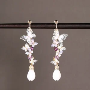 Amethyst butterfly drop Chinese earrings displayed from the front with translucent purple butterflies, clustered violet beads, white teardrop pendants and gold-tone ear wires