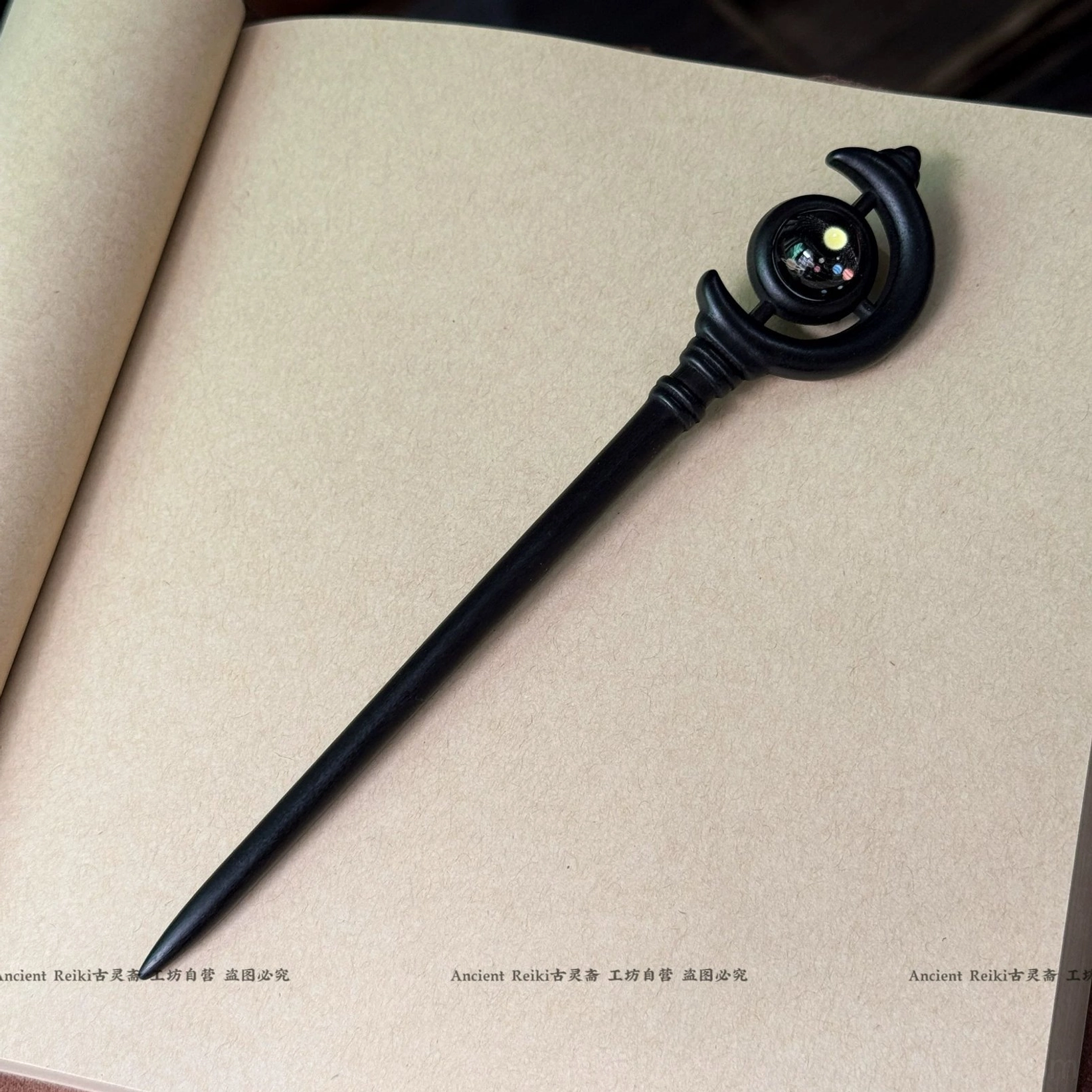 Ancient Chinese black wooden hair stick with smooth slender design, crescent-shaped top, and yellow-accented glass bead on a kraft notebook
