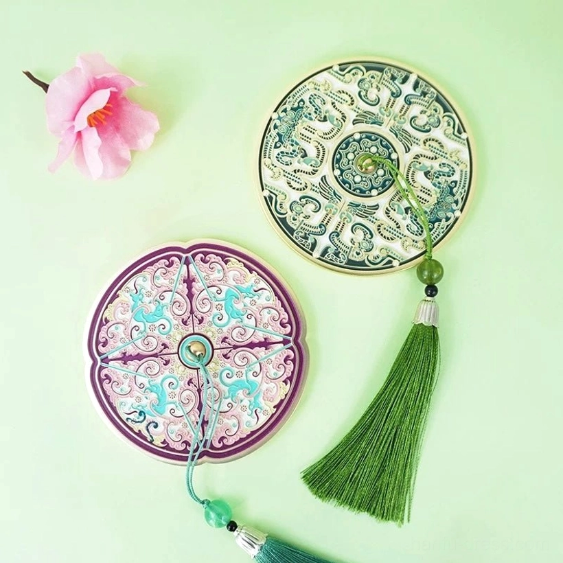 Ancient Chinese bronze mirror-inspired pocket mirrors in Jade green and Amethyst purple designs displayed on a light green background with a pink flower ornament