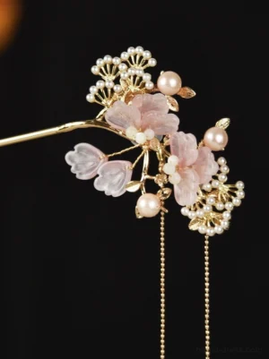Front view of an ancient Chinese style flower hair stick with asymmetric pink floral ornaments, clustered pearl decorations, gold-toned details, and long hanging tassel chains