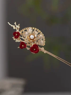 Ancient Chinese style plum blossom hair stick shown in close-up with a golden fan ornament, red floral details, central pearl, and sparkling crystals