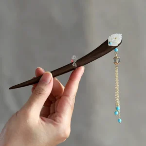 Handheld view of an ancient Chinese style wooden hair stick featuring a white petal ornament, blue beads, and a flowing golden chain tassel