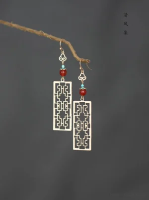 Antique Chinese Hanfu drop earrings with gold tone hollow window pendant, red agate and turquoise beads, cloud shaped accents, comfort clip on style displayed on a dark gray background