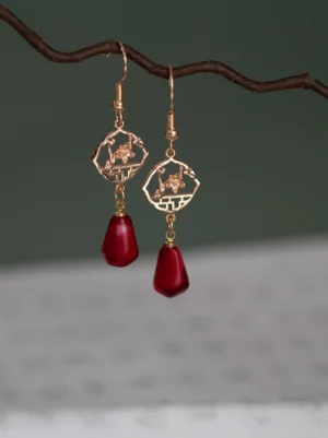 Comfort clip-on antique Chinese window flower drop earrings with hollow gold floral lattice charms and wine-red teardrop pendants displayed on a natural branch