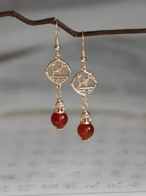 Antique gold Chinese window flower earrings with openwork floral lattice charms and round red agate-style pendants against traditional calligraphy paper