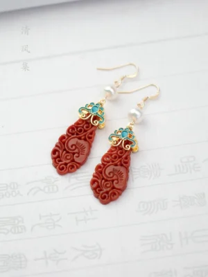 Antique red jade cloud drop earrings with blue filigree ornaments and pearl-like beads on traditional Chinese calligraphy paper