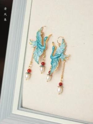 Antique-inspired turquoise cloisonne crane pearl tassel earrings displayed on a linen backing with red agate beads and gold-tone chains