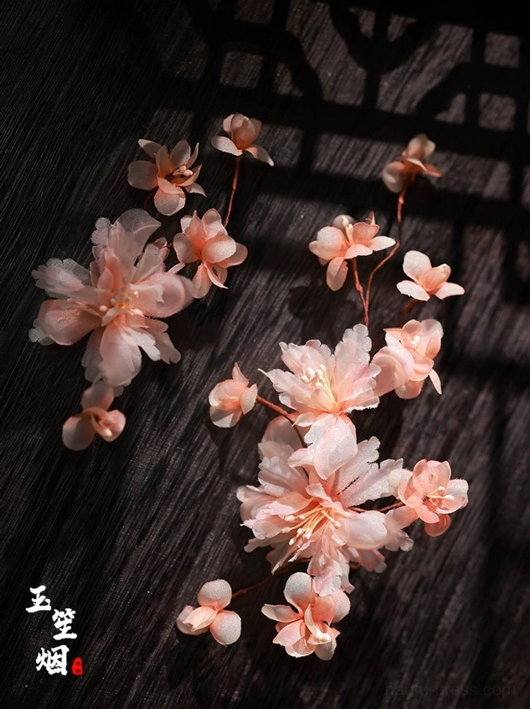 Flat lay of light pink simulated apricot blossom hair ornaments with brown branches displayed against dark hair and Chinese window shadows