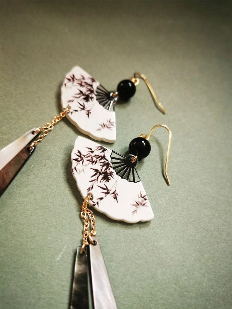 Close-up of asymmetric black and brown bamboo fan earrings with black round beads, gold hooks, and elegant dual-tone metal tassels