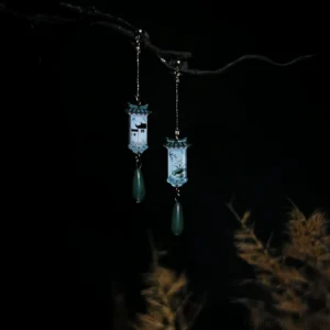 Asymmetrical Chinese cottage dangle earrings for Hanfu featuring traditional pendants, green teardrop charms, gold-toned chains, and vintage-inspired metal details displayed on a dark branch