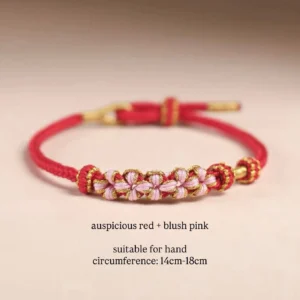 Handwoven auspicious red Chinese knot flower bracelet with blush pink flower knots and gold-tone accents on a warm studio background