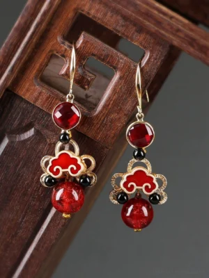 Close-up of auspicious ruby cloud cheongsam earrings with traditional Chinese cloud motif on vintage carved wood background