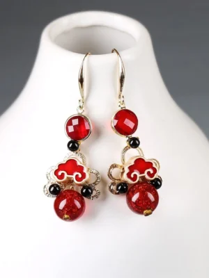 Auspicious ruby cloud Chinese earrings with red enamel cloud charms gold tone hooks and dangling red beads on white jewelry holder