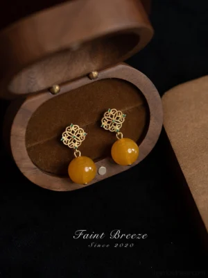 Traditional Chinese amber-colored bead drop earrings with gold floral filigree tops and green gemstone accents displayed inside a vintage wooden jewelry box