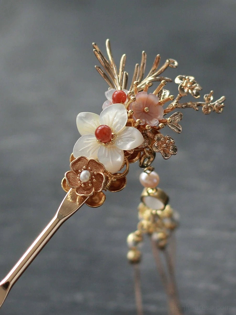 Close-up of an autumn blossom Chinese hair stick with gold floral branches, white and pink flowers, red flower centers, and a beaded crystal tassel on a dark slate background