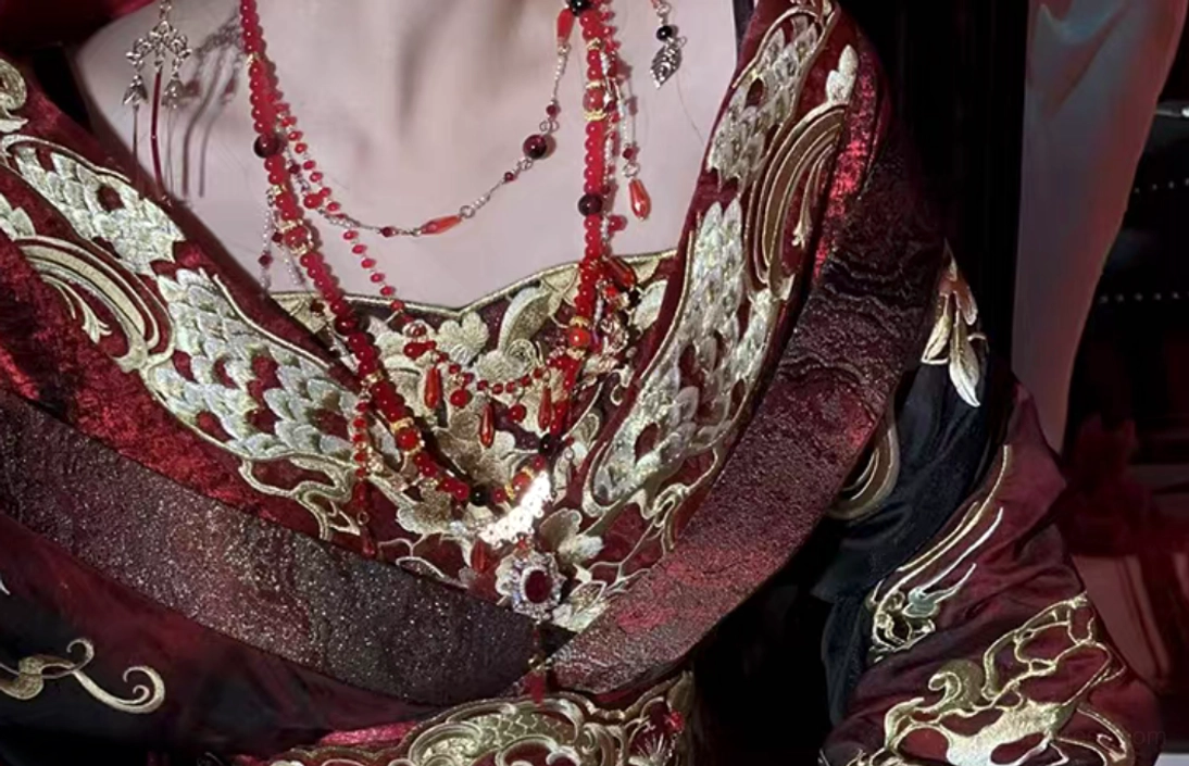 Close up of wine red cross collar Hanfu with heavy gold embroidery layered red bead necklaces pendants and detailed textile texture