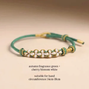 Handwoven Chinese knot bracelet in autumn green with cherry blossom white floral details and gold-tone accents, adjustable drawstring design shown on a warm neutral background