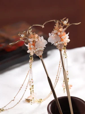 Pair of traditional Chinese hair sticks with pink and white floral clusters, pearl accents, gold-toned branches, layered tassel chains, and flower pendants displayed on white fabric