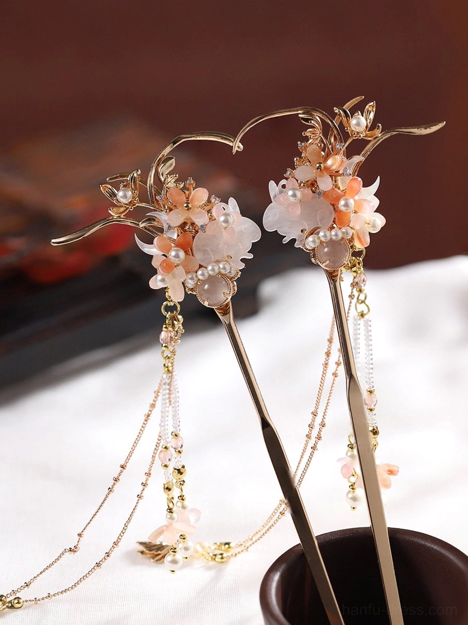 Pair of traditional Chinese hair sticks with pink and white floral clusters, pearl accents, gold-toned branches, layered tassel chains, and flower pendants displayed on white fabric