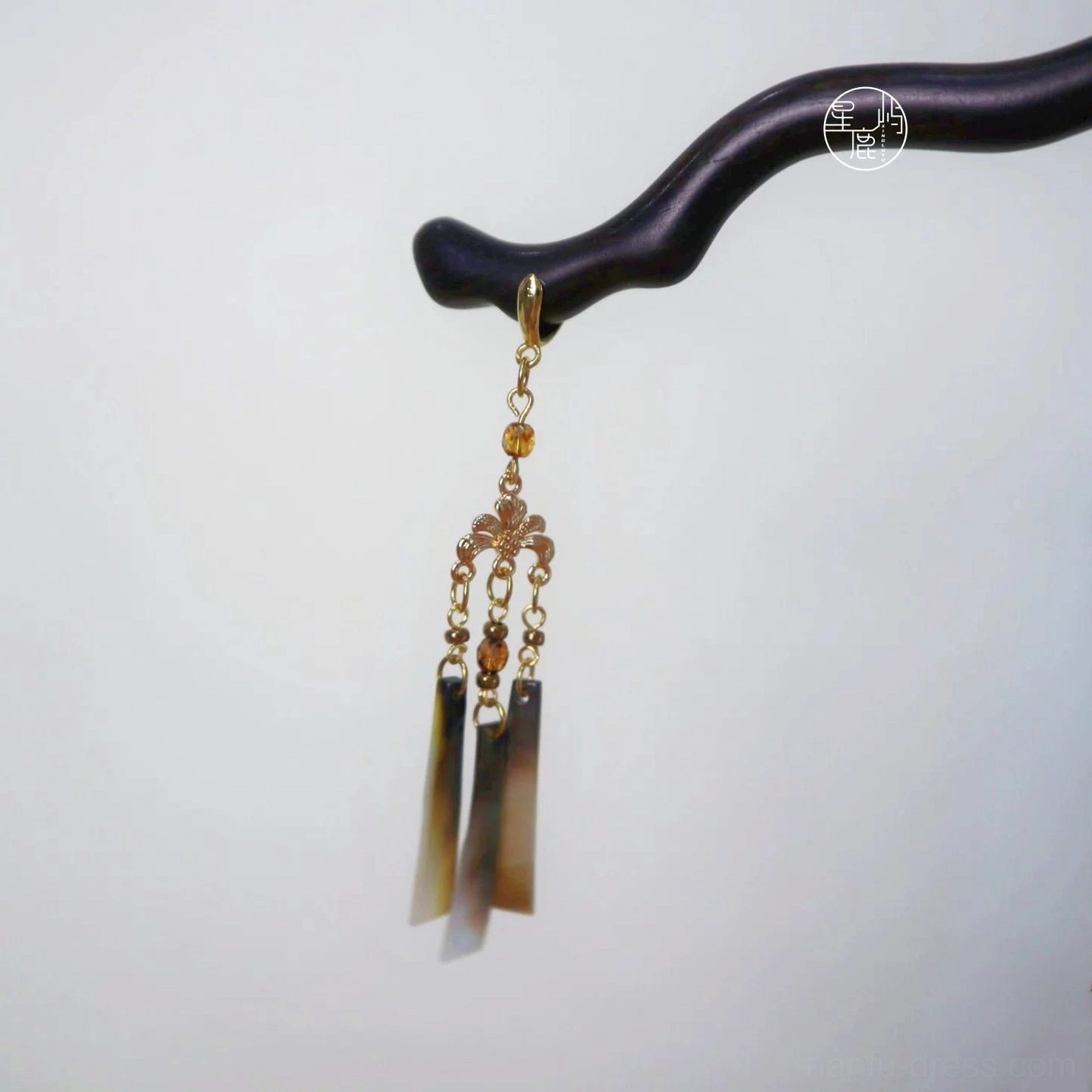Close-up of an autumn-inspired Chinese hair stick with dark brown wavy wood, gold filigree, brown beads, tassel, and shell pendants