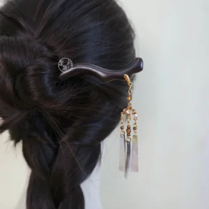 Woman wearing a traditional Chinese dark wooden hair stick with gold-tone details, beaded tassel, and shell pendants in a braided updo