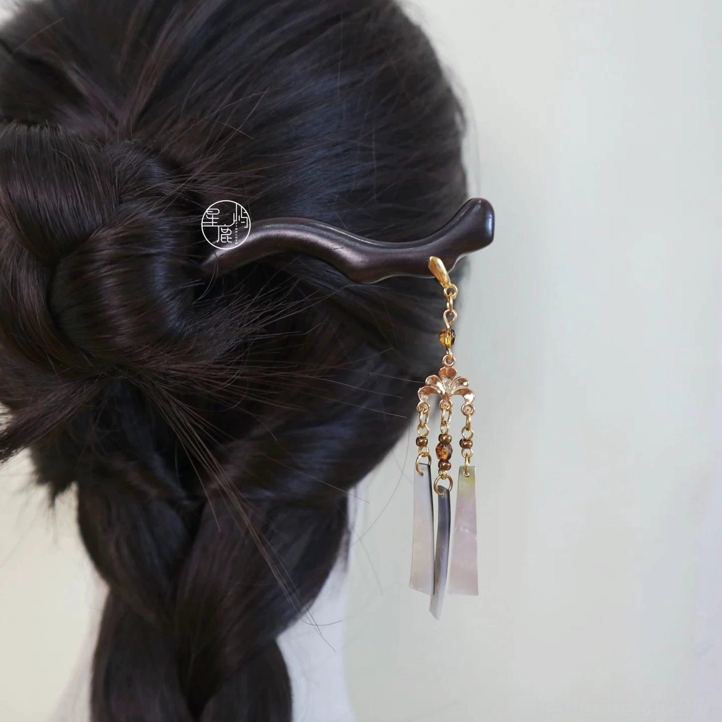 Woman wearing a traditional Chinese dark wooden hair stick with gold-tone details, beaded tassel, and shell pendants in a braided updo