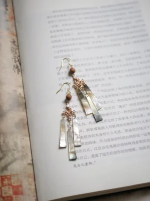 Autumn Wind iridescent shell drop earrings with rose gold carved connectors and light brown wooden beads displayed on a classical Chinese book, handcrafted Hanfu Chinese jewelry
