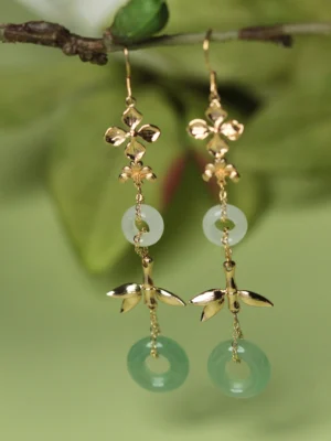Traditional Chinese dangle earrings displayed on a tree branch with gold floral tops bamboo pendants white ring charms and green aventurine accents