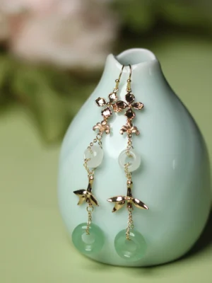 Aventurine green ring Chinese earrings with gold flower links bamboo charms and white jade-tone circular pendants beside a pale cyan vase