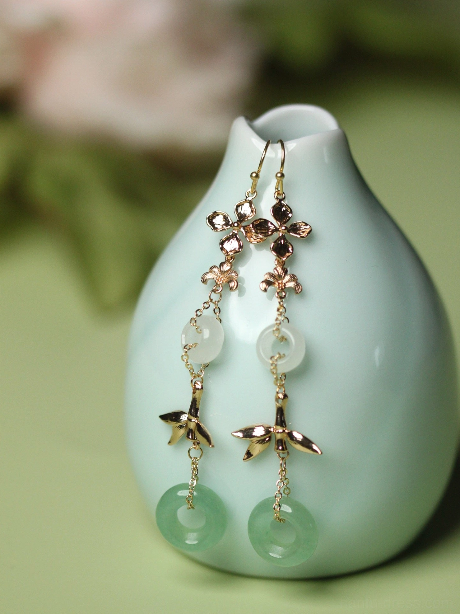 Aventurine green ring Chinese earrings with gold flower links bamboo charms and white jade-tone circular pendants beside a pale cyan vase