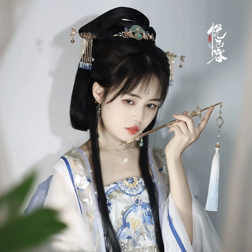 Hanfu model holding a long tassel Chinese hairpin while wearing coordinated ancient style hair ornaments and blue white costume