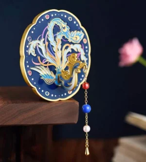 Azure fenghuang Chinese hand mirror displayed on a wooden shelf with gold phoenix artwork, midnight blue decorative back, and red blue pearl-like beaded tassel