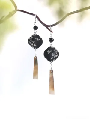 Bamboo leaf plum blossom Chinese dangle earrings with black floral charms, silver bamboo pattern and iridescent shell tassels displayed on a natural branch