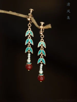 Close-up view of Chinese bamboo drop earrings with blue green enamel leaves pearl beads red pendants and hook ear wires