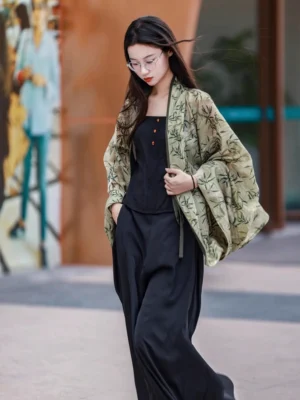 Side three quarter view of a loose bamboo printed Hanfu cardigan styled with a black camisole and wide leg trousers in an urban street setting