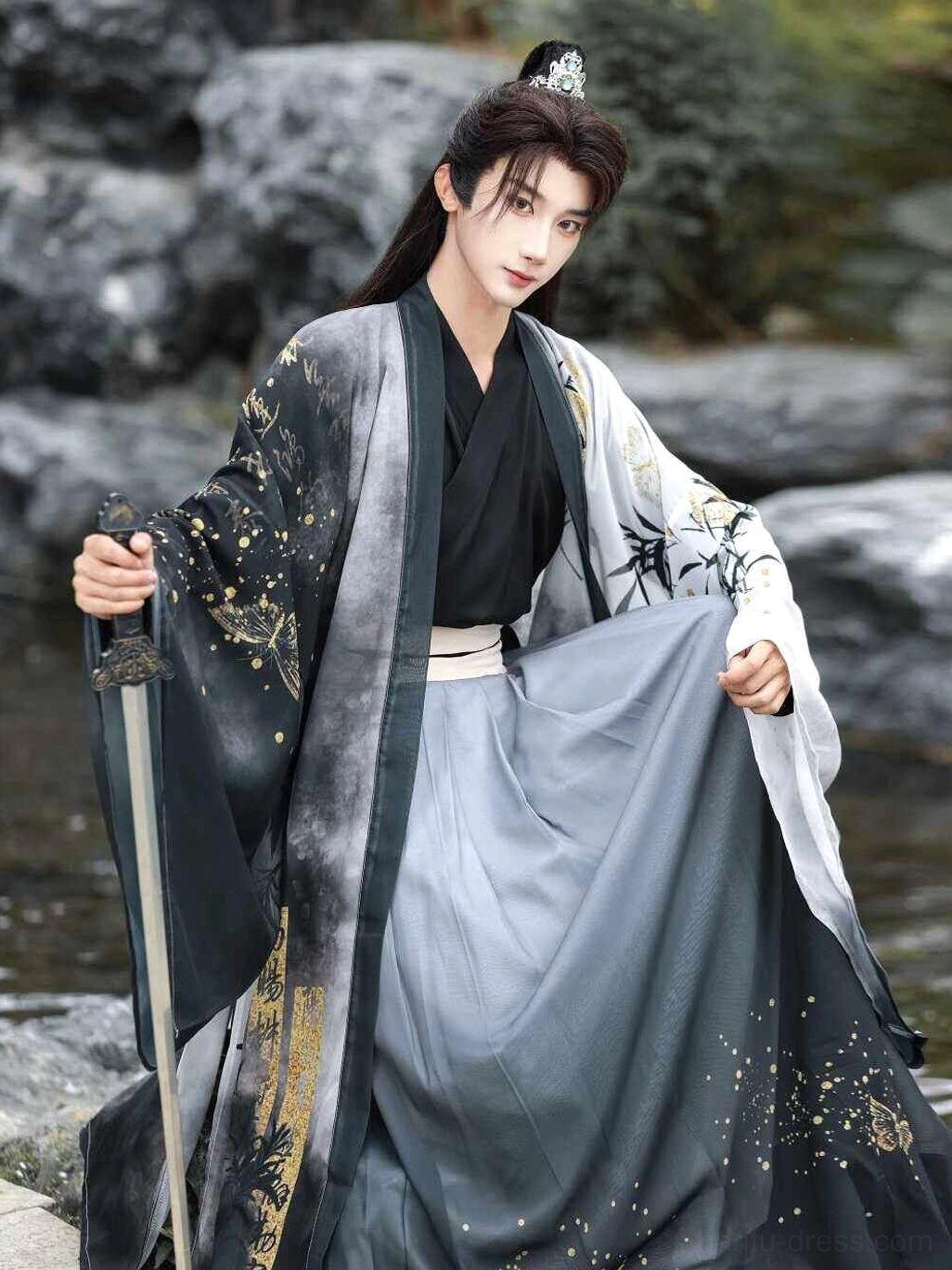 Close three-quarter view of men’s Xianxia hanfu robe showing bamboo and gold sleeve decoration, wide lapel, and ink-wash gradient pleated skirt