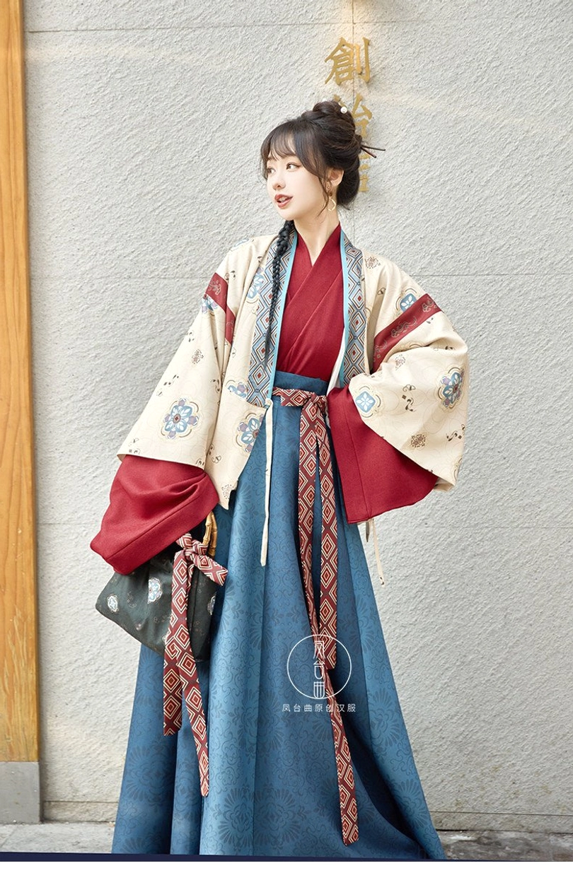 Beige and blue modern hanfu outfit with cropped outer jacket, layered red sleeves, flowing high-waisted skirt, and long geometric waist sash