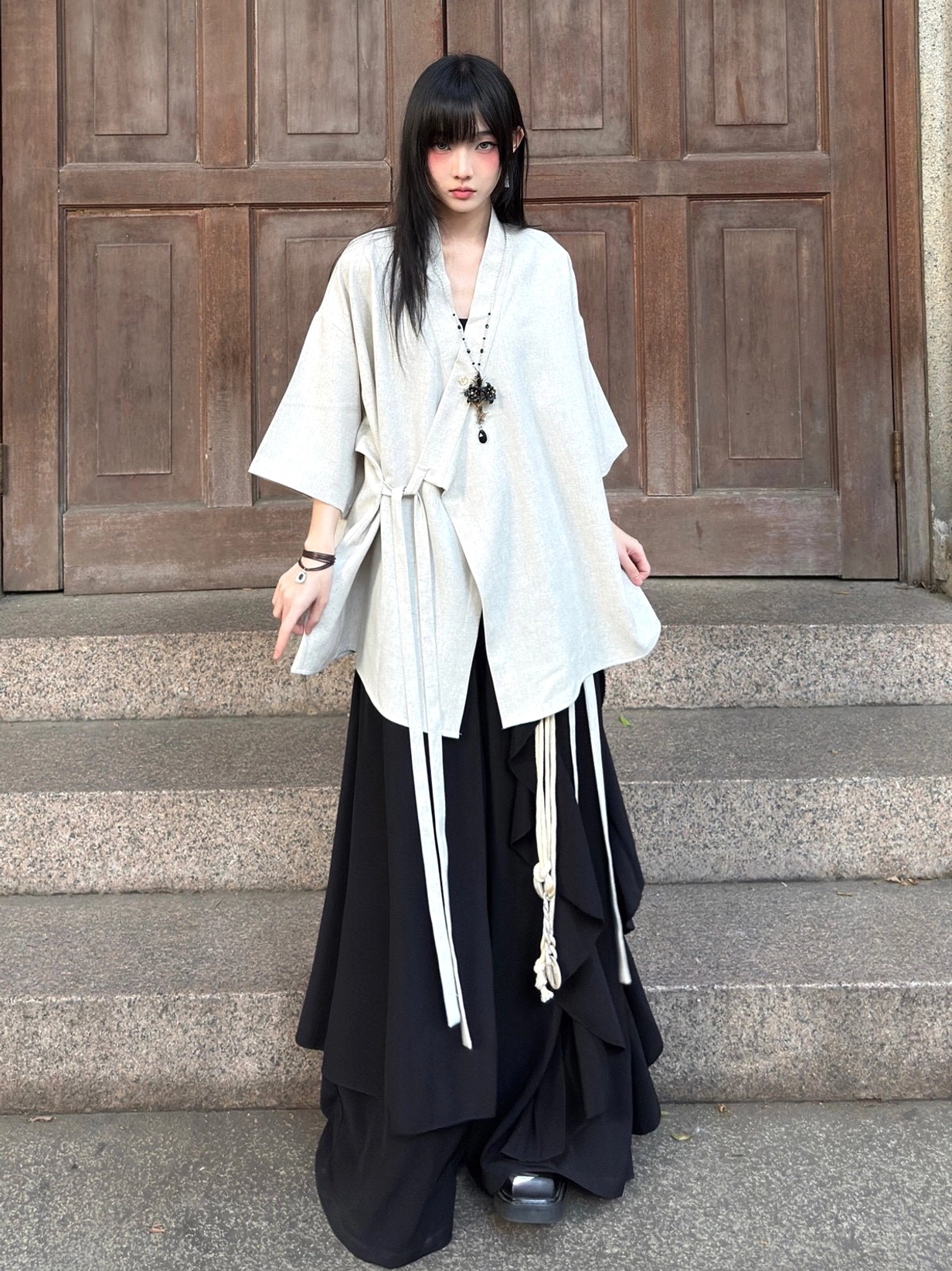 Off-white beige modern Hanfu cross-collar cardigan with decorative front tie straps styled with black layered wide-leg pants