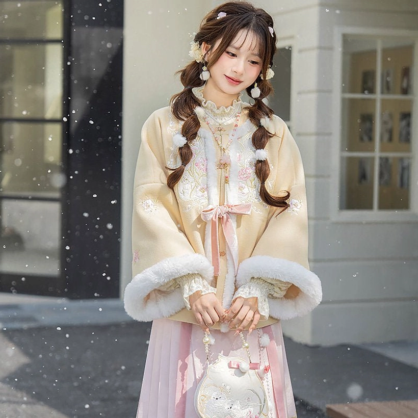 Bust up view of beige winter Hanfu jacket with fluffy cuffs, embroidered stand collar, pink ribbon bow, and traditional Ming style detailing
