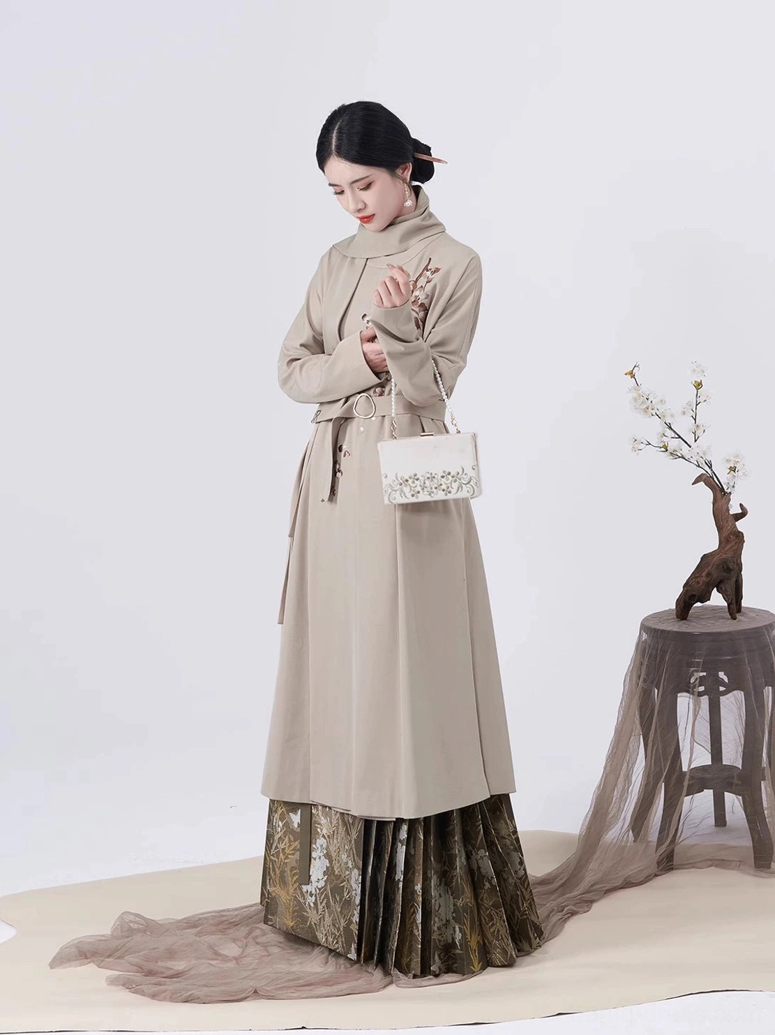 Front view of belted taupe Ming Dynasty-inspired Hanfu long coat with dark gold patterned pleated mamianqun skirt and detachable mini bag