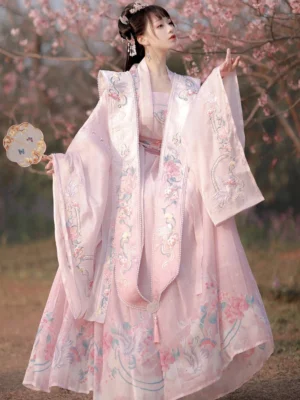 Three-quarter front view of a soft pink Birds and Flowers Song Dynasty style qiyao ruqun Hanfu with floral and phoenix embroidery, pearl-trimmed collar, wide sleeves, and round fan in a cherry blossom garden