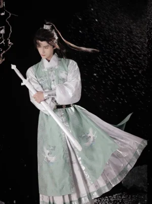 Three-quarter view of male Ming Dynasty inspired crane hanfu robe with flowing green skirt and white sword in snowy studio