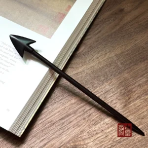 Matte black arrowhead Chinese wooden hair stick displayed on an open book and wood grain table for Hanfu hair styling